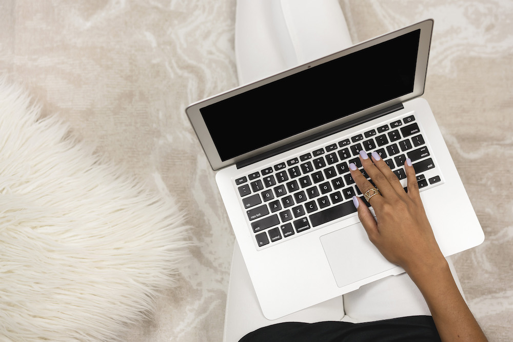 Female hands typing on a laptop computer on a white fuzzy bedspread