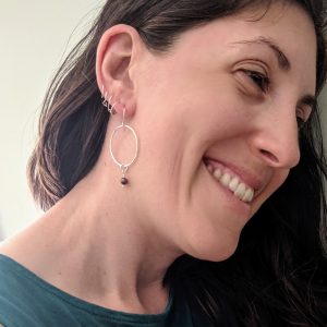 Picture of the creator's profile, showcasing an ear with four huggie hoop earrings and a dangly hoop earring with a small bead hanging from the bottom. 