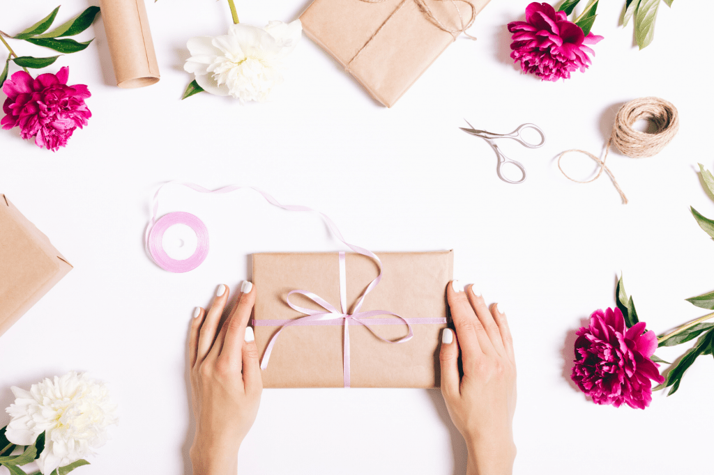 hand holding wrapped gift with scissors and flowers around the gift
